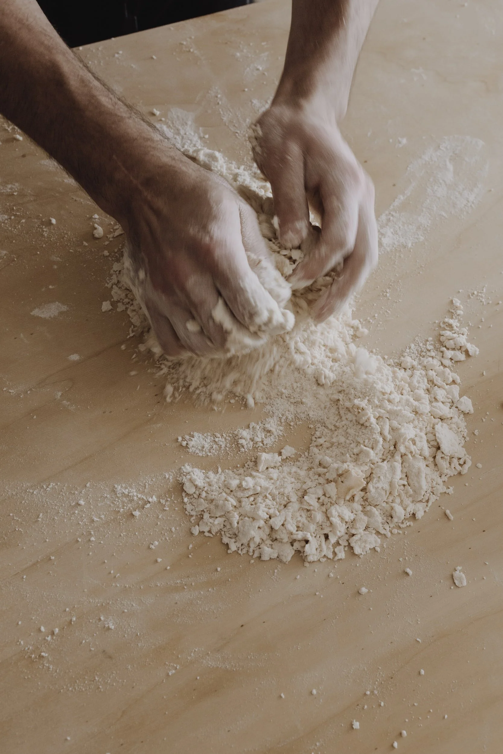 Hands kneading dough on a wooden surface.