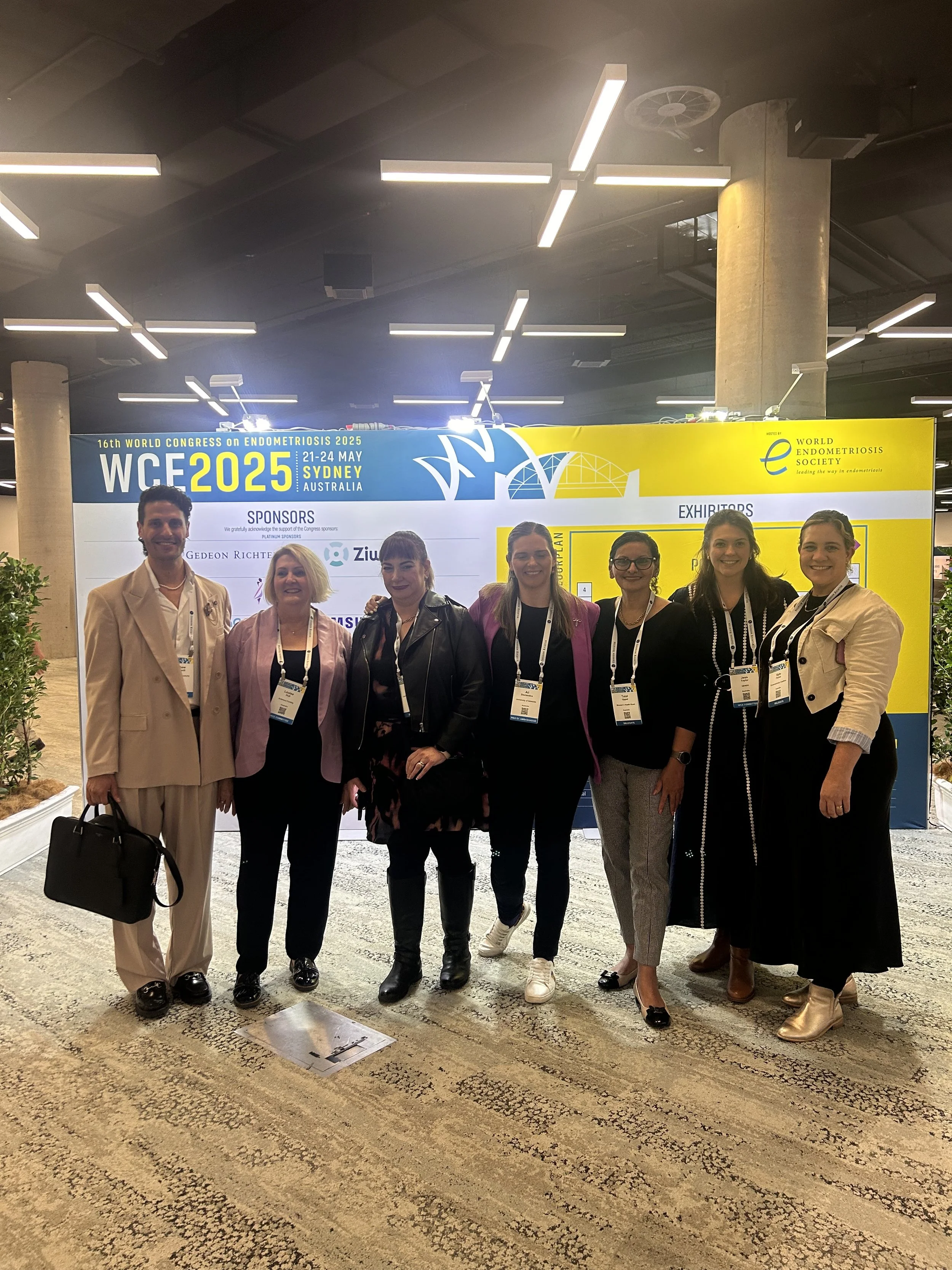 Group of seven people standing in front of a conference sign at the 16th World Congress on Endometriosis 2025 in Sydney, Australia. They are dressed professionally and wearing conference badges.
