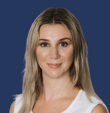 A young woman with shoulder-length blonde hair wearing a white top, smiling at the camera against a solid dark blue background.