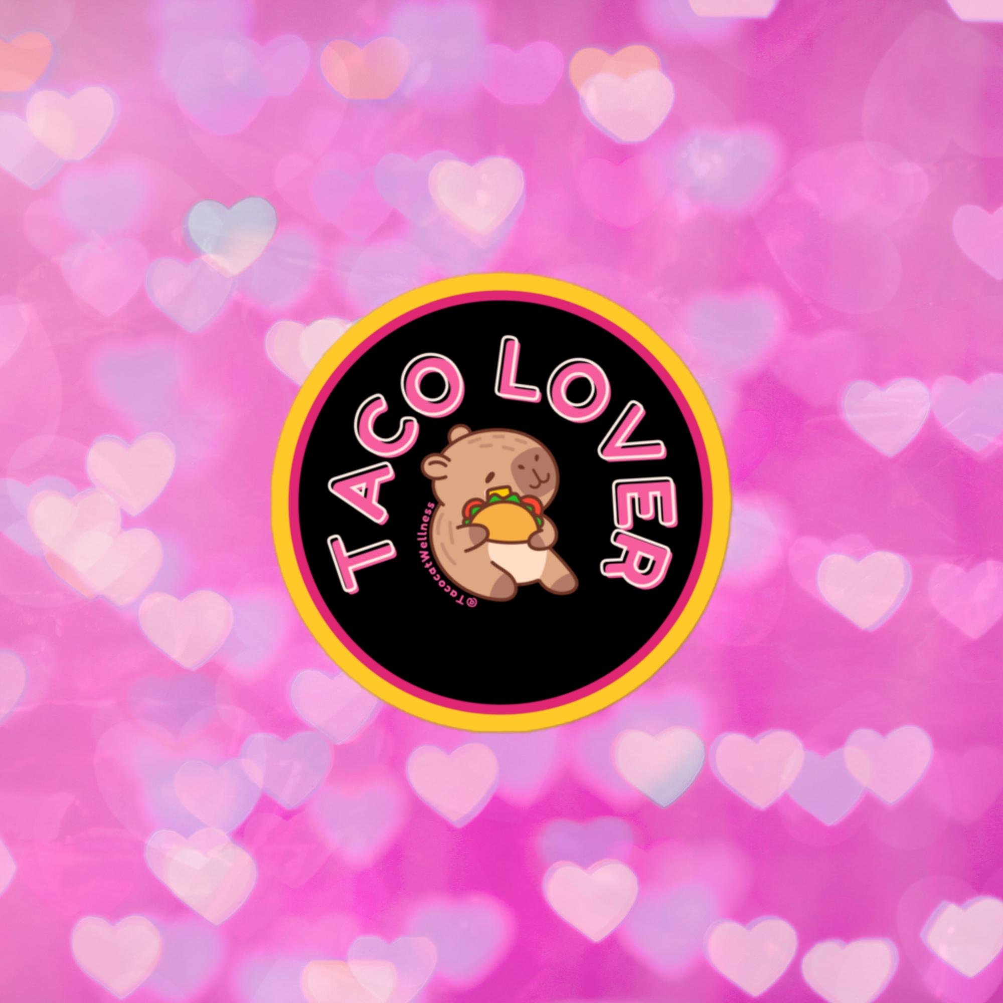 Round sticker with a black background and bold pink border, featuring a cartoon capybara holding a taco with a satisfied smile. “Taco Lover” curves around the image in pink and white block letters.
