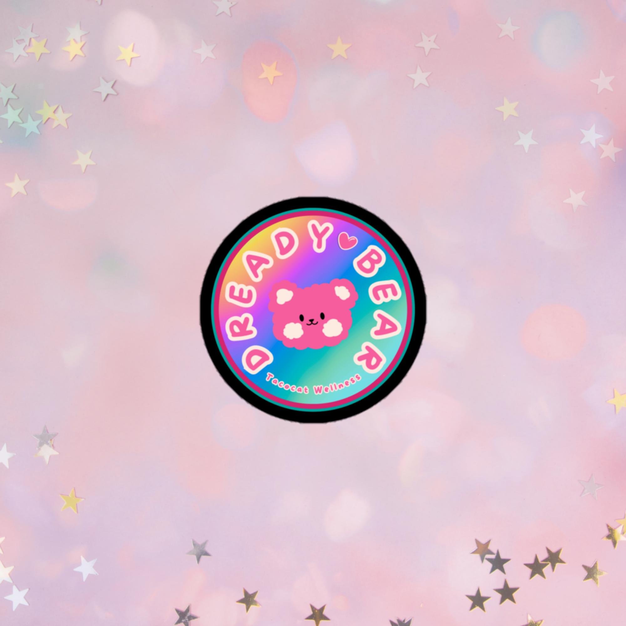 pastel rainbow background featuring a fluffy pink bear with soft cream-colored cheeks. The text around the top reads “Dready Bear”