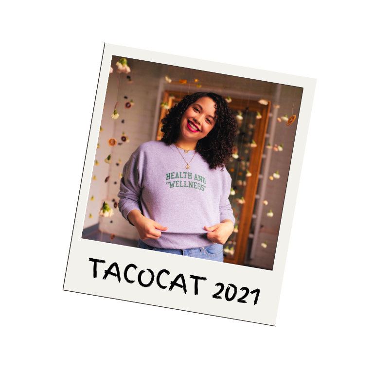 Polaroid style photo of Angela, smiling, wearing a "health and wellness" sweatshirt against a hanging flower background