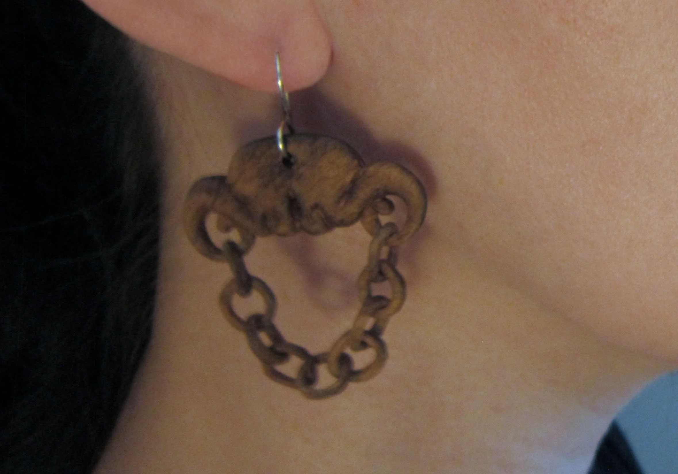 A model wearing a hand carved wood chain earring with a sterling silver french hook ear wire.