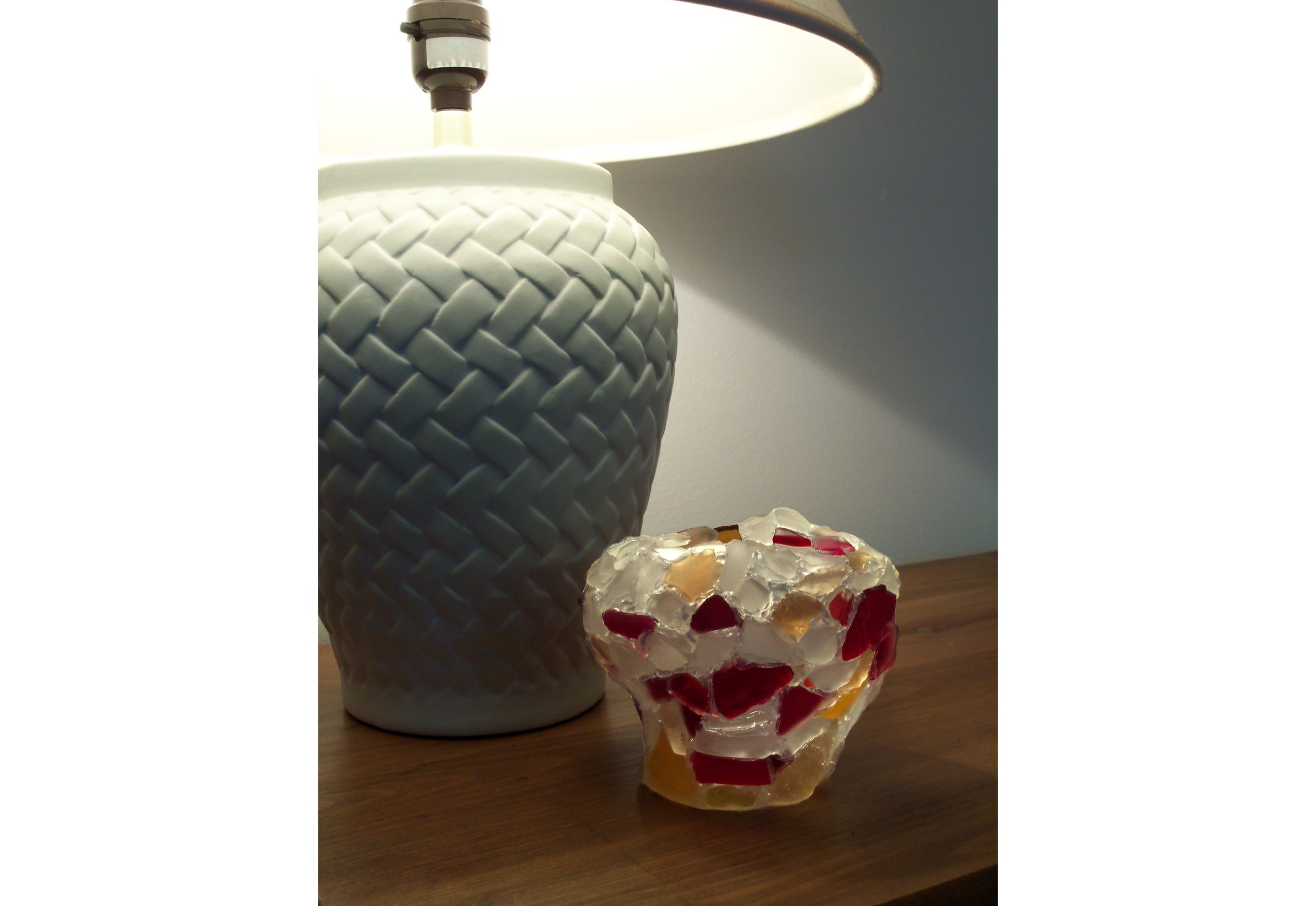 An abstract red, yellow, & white recycled glass bowl sculpture next to a lamp.