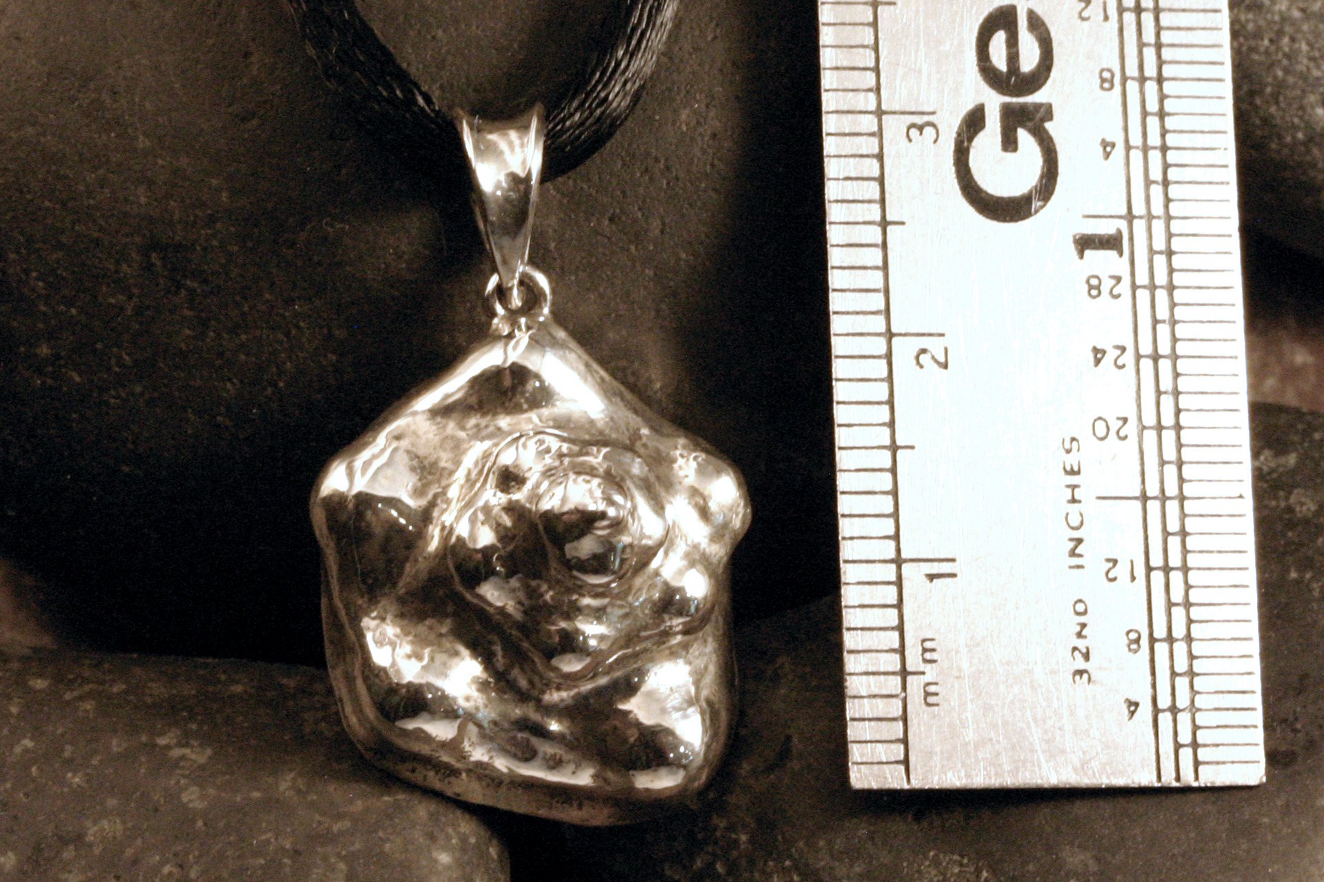 A medium sterling silver conch shell pendant next to a ruler.