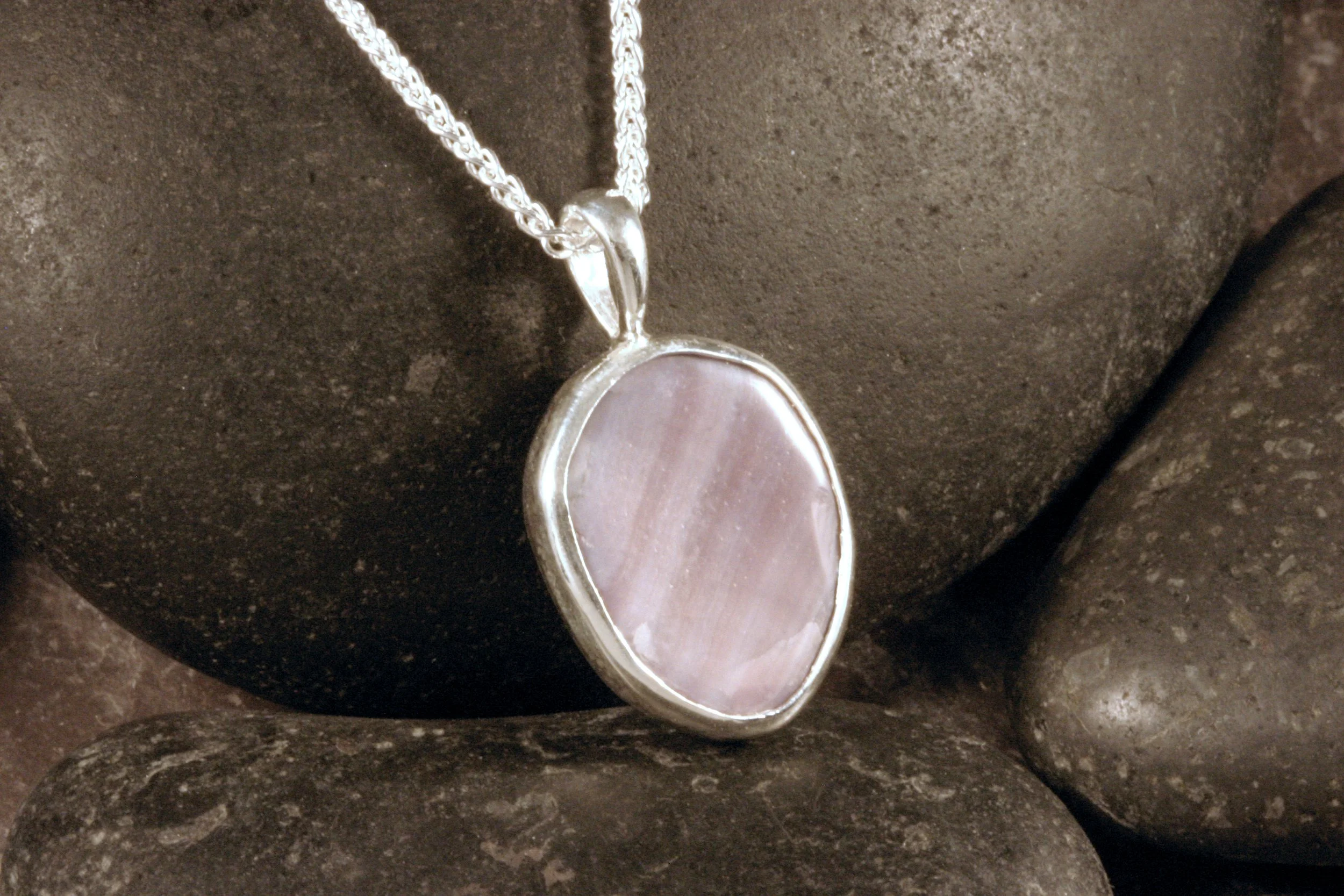 An angled view of a sterling silver polished wampum shell pendant.
