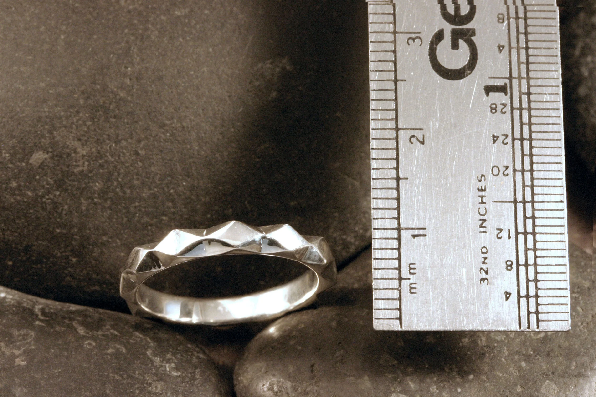 A sterling silver geometric diamond band next to a ruler for a size reference.