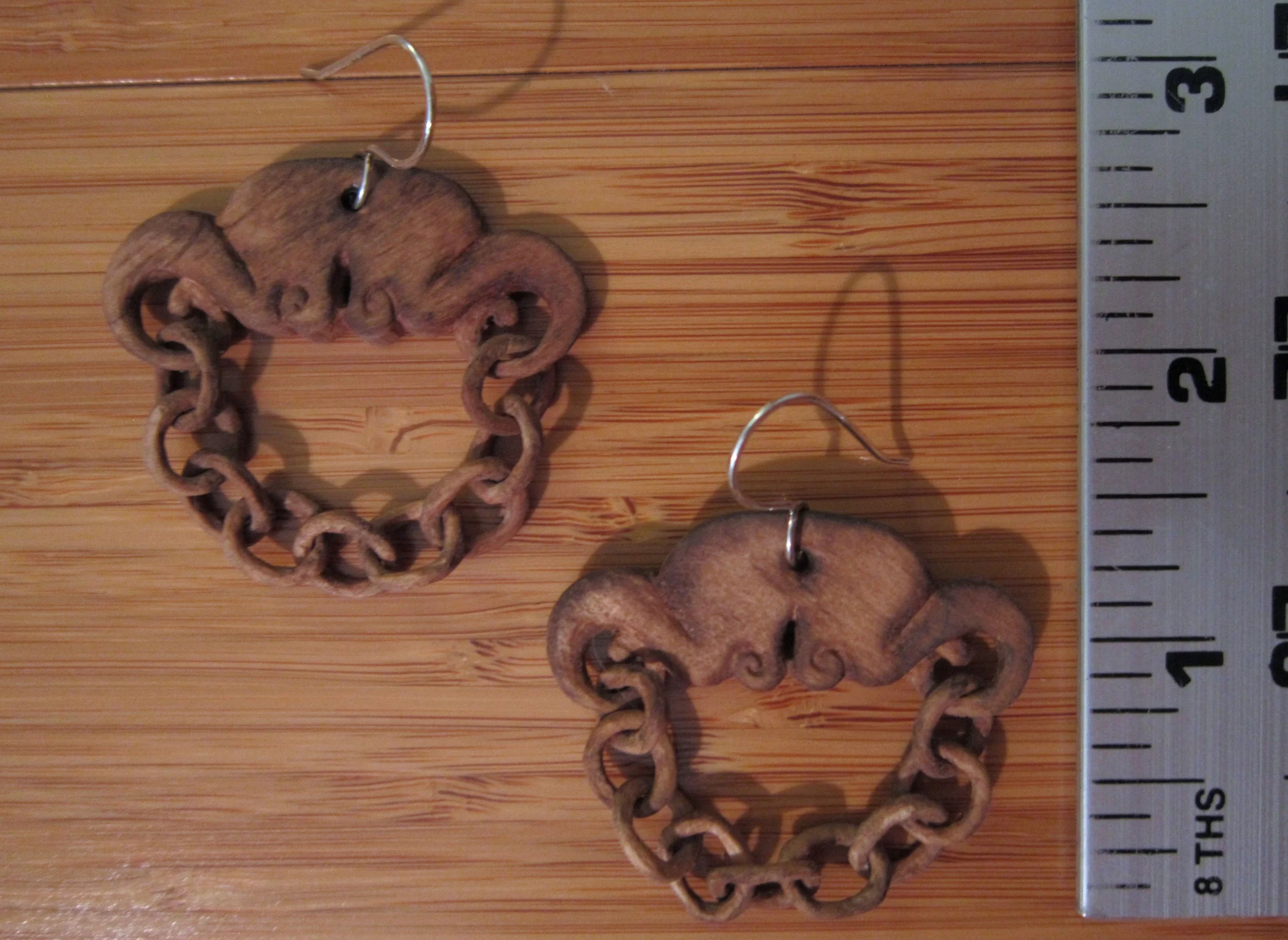 Hand carved wood chain earrings next to a ruler.
