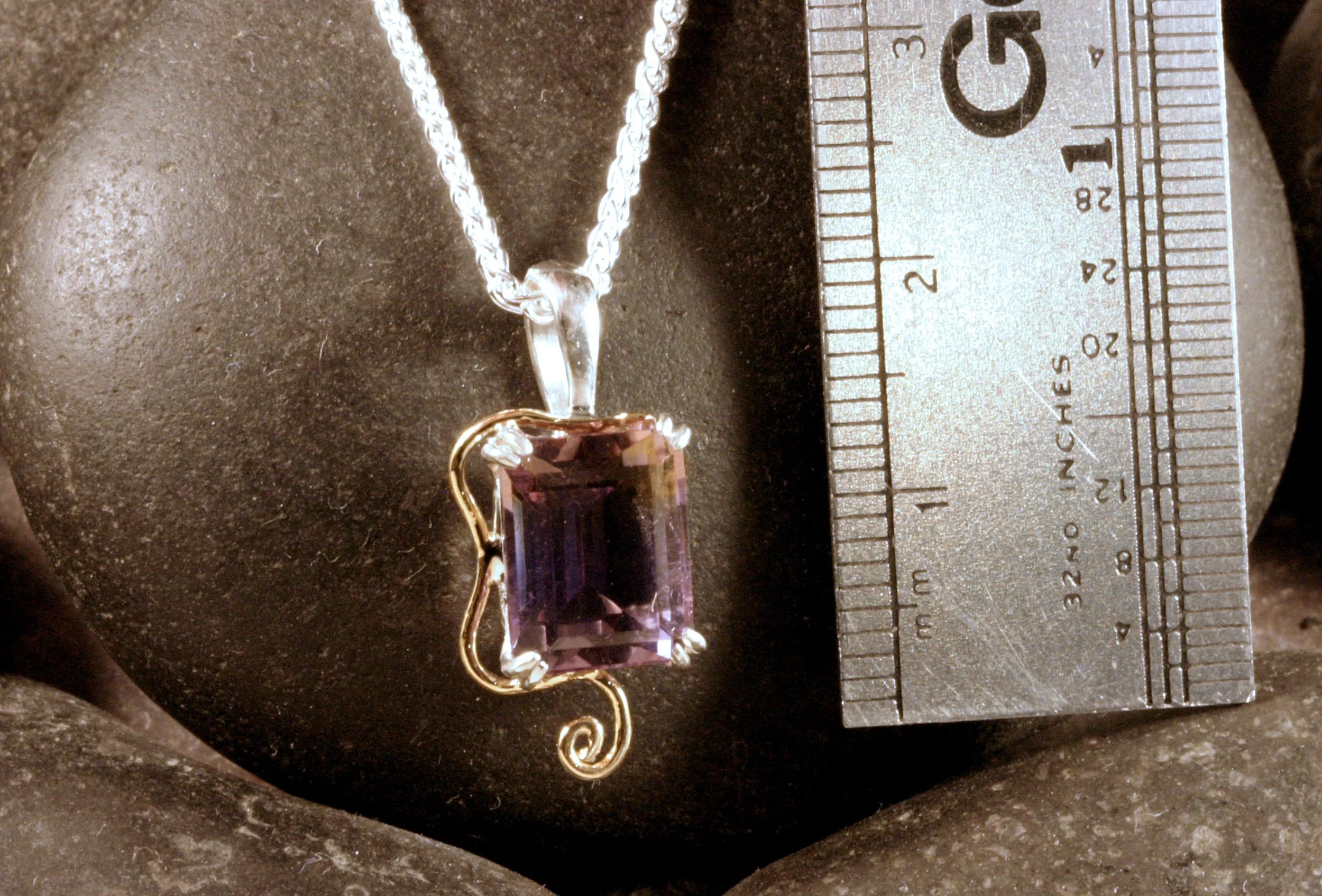 A sterling silver & 14K gold ametrine pendant next to a ruler for a size reference.