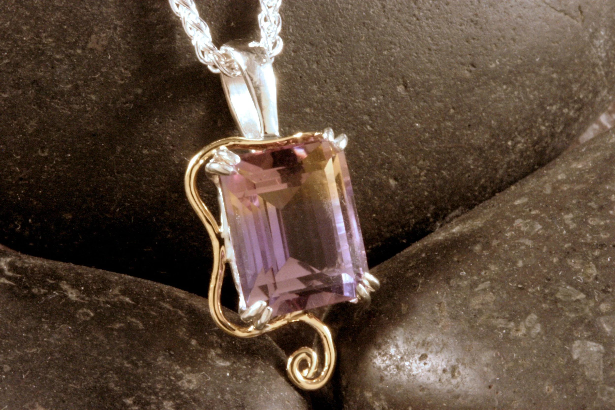 A close up of a sterling silver & 14K gold ametrine pendant with a wavy swirl accent.