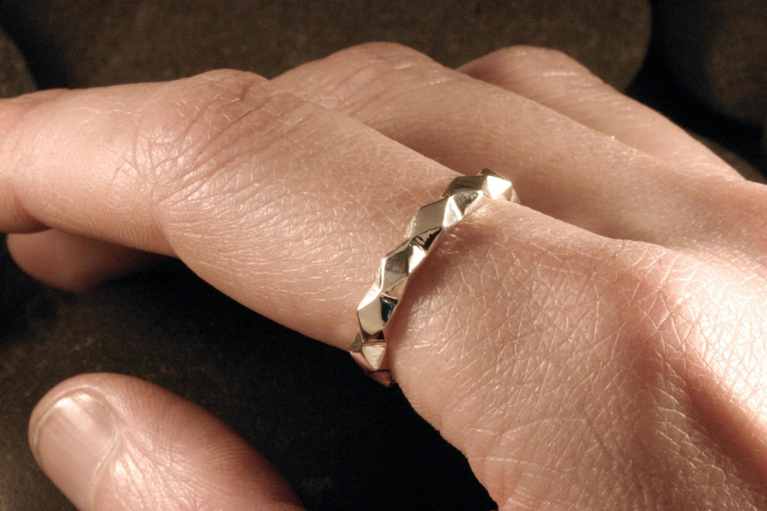A model's hand with a sterling silver geometric diamond & triangles patterned band on her index finger.