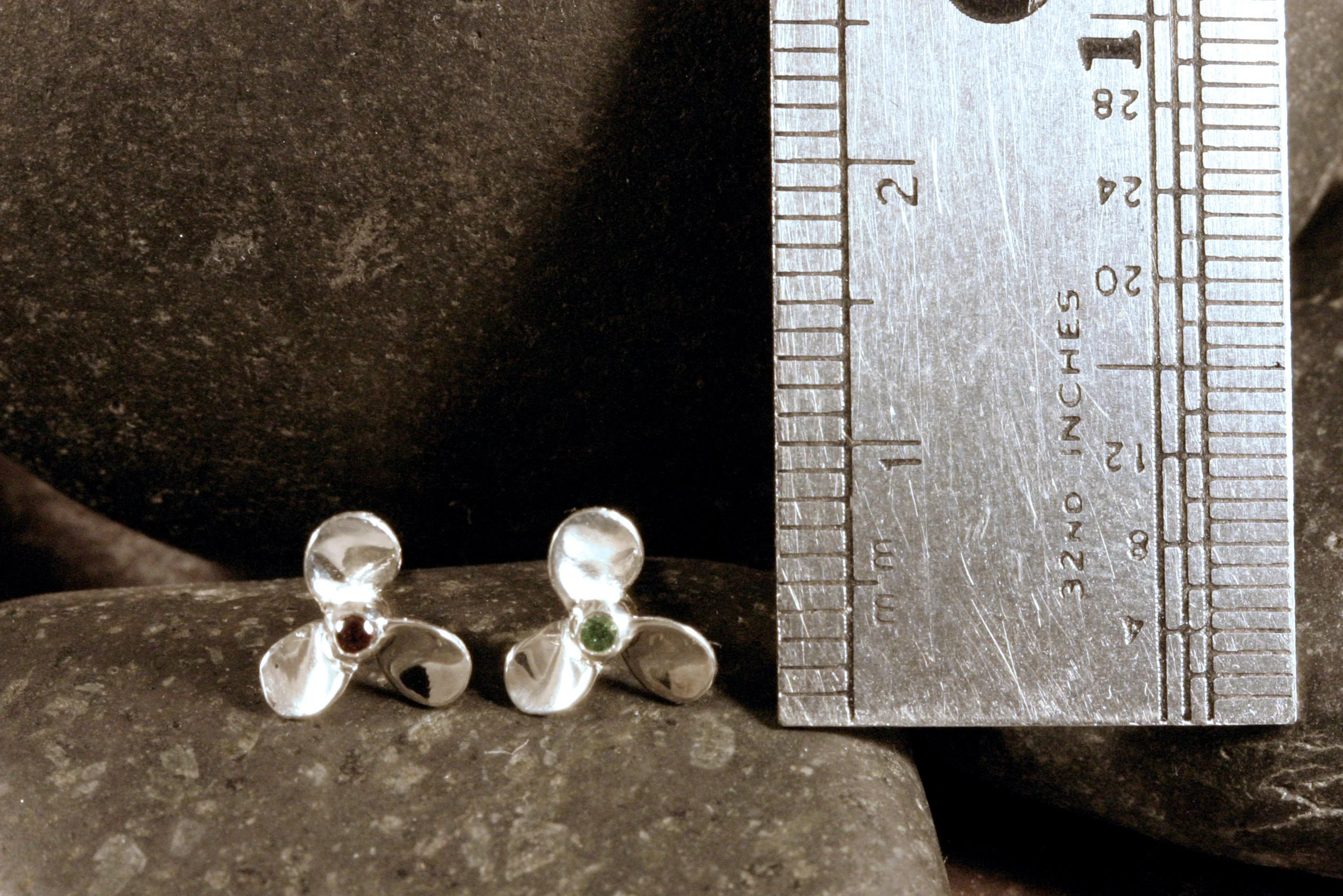 Mini propeller stud earrings in sterling silver with red & green garnets  next to a ruler for a size reference.