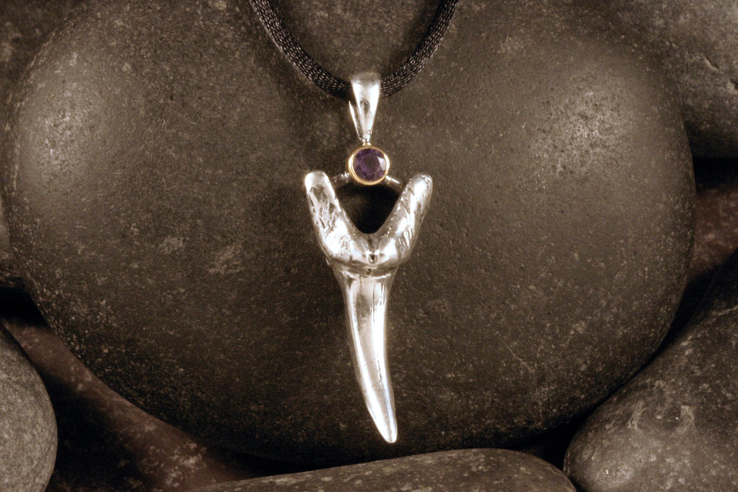 A front view of a sterling silver and 14K gold fossil shark tooth pendant with an amethyst.