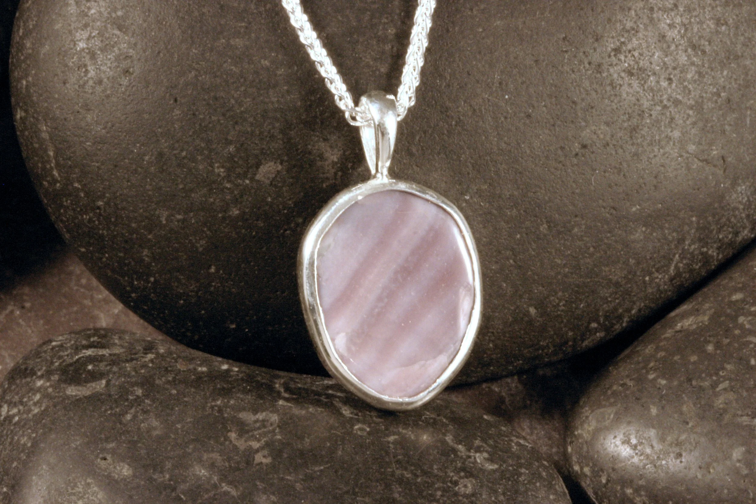 A sterling silver bezel set polished wampum shell pendant with natural stripes of purple and white on the shell.