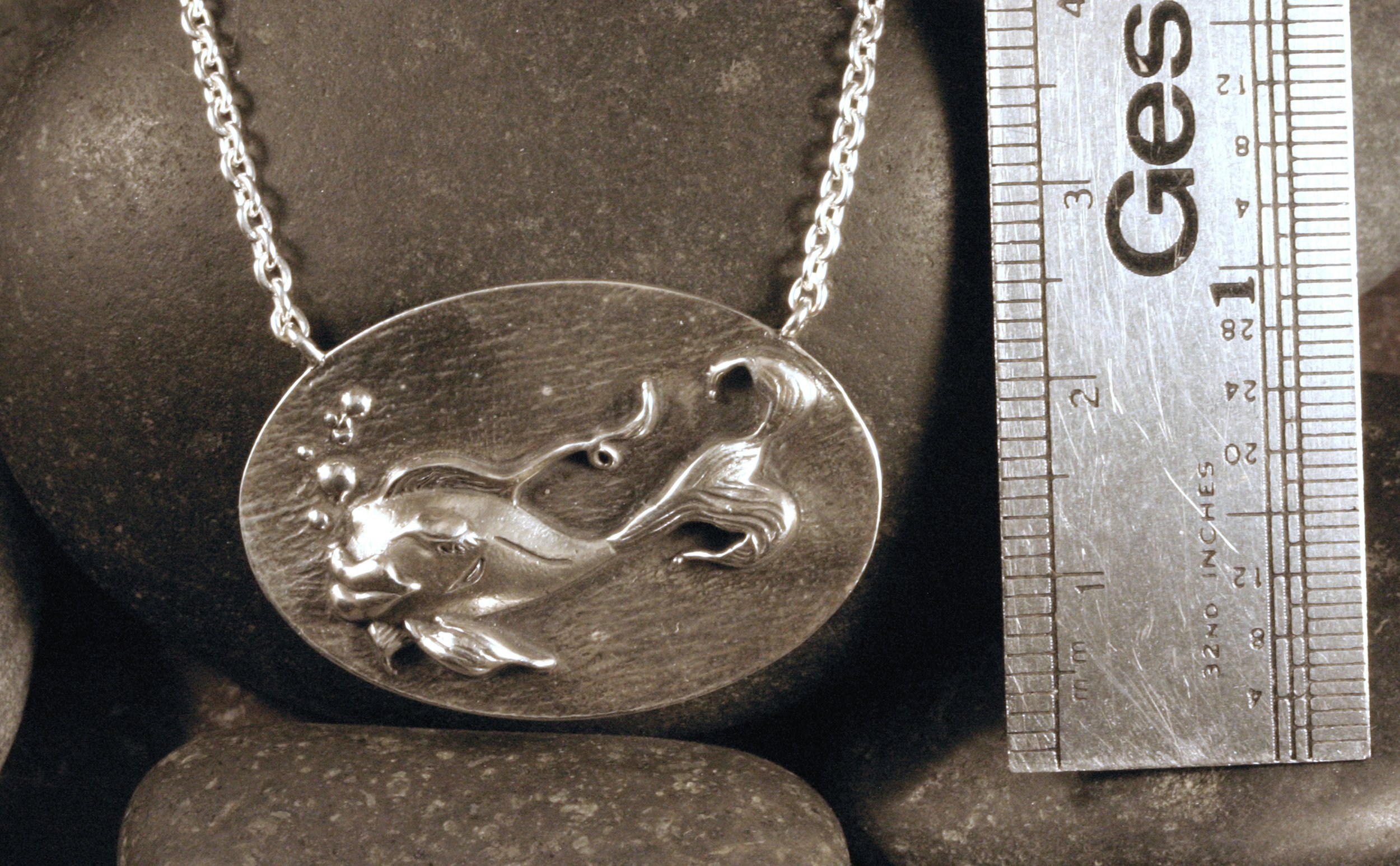 A sterling silver fish necklace next to a ruler for size reference.