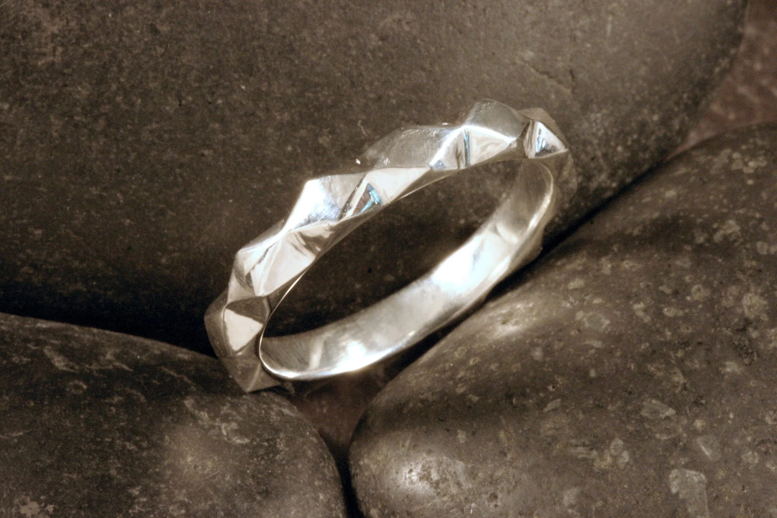 A three quarters view of a sterling silver geometric diamond pattern band.