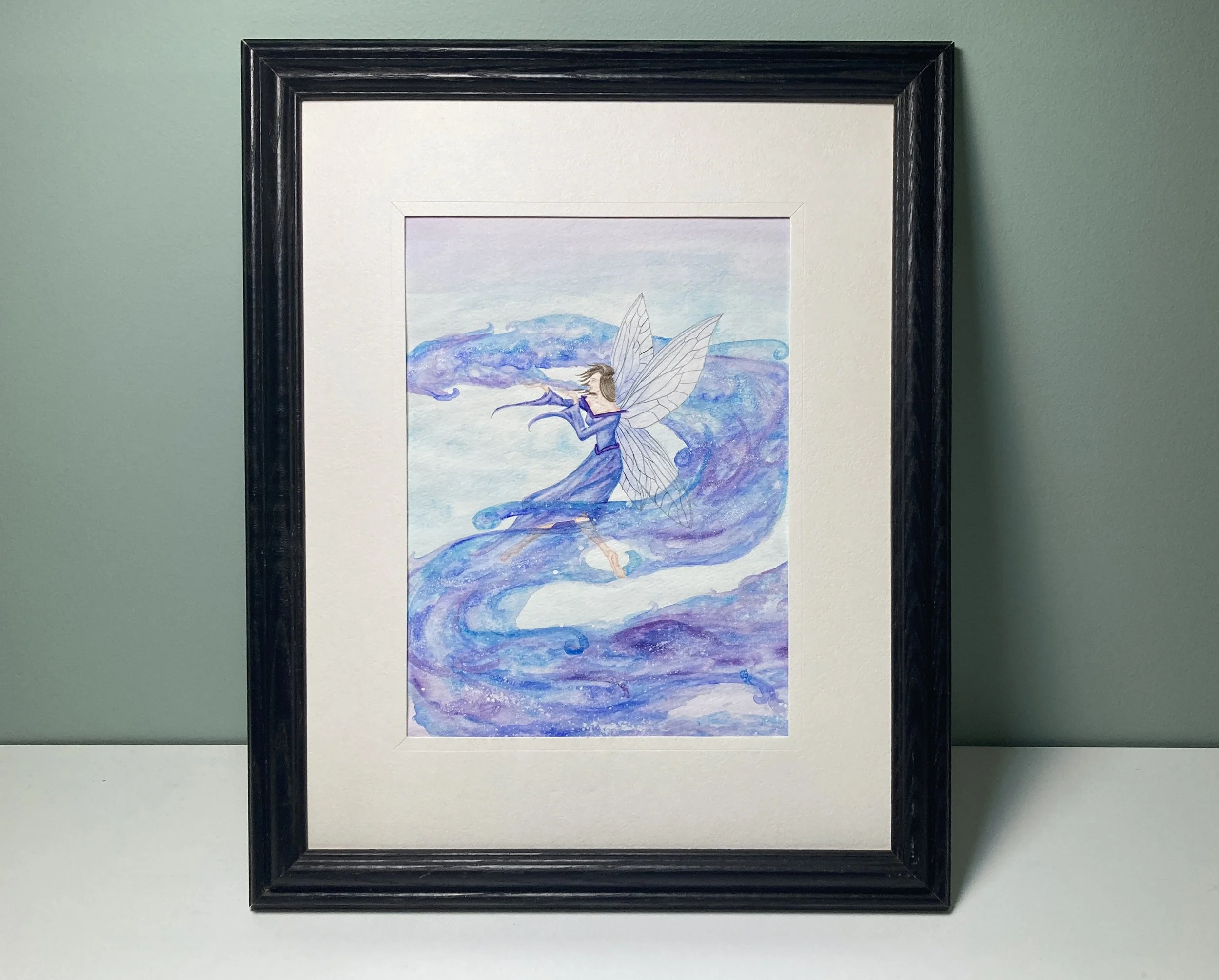A framed watercolor painting of a fairy blowing out dream clouds that are swirling around her.