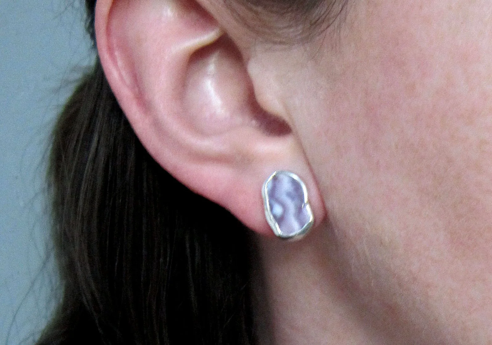A model wearing small sterling silver wampum freeform pentagon studs.