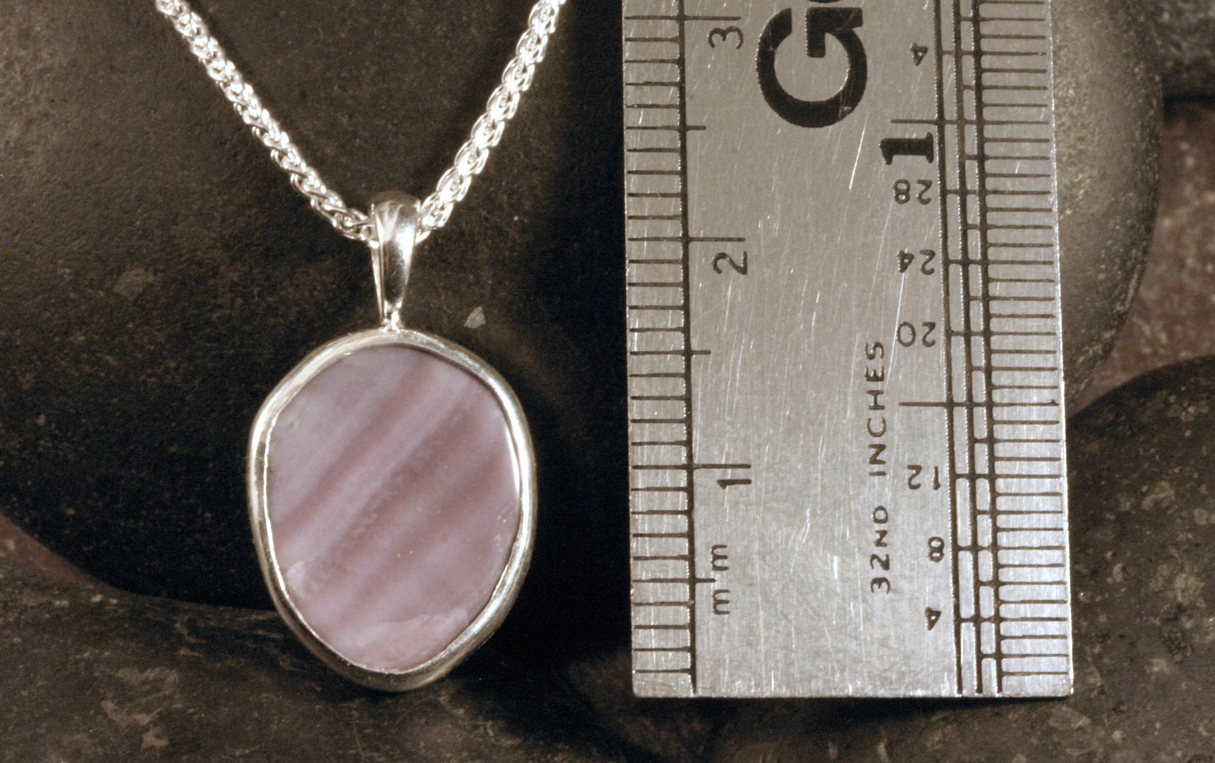 A sterling silver wampum seashell pendant next to a ruler.