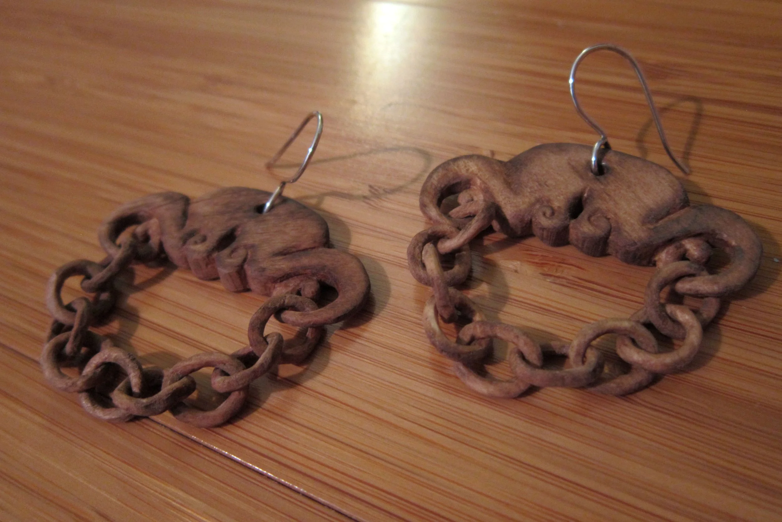 An angled view of hand carved wood chain earrings with sterling silver ear wires.