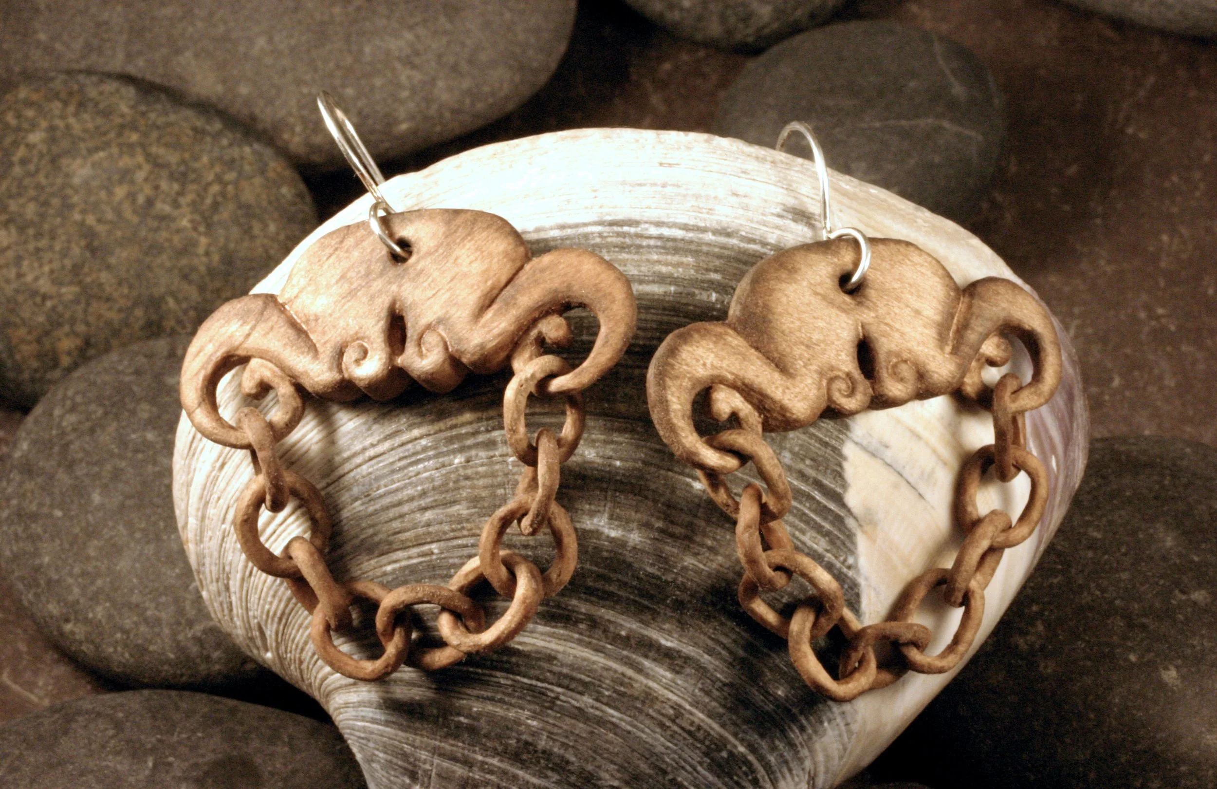 Handcarved wood earrings with sterling silver ear wires draped over a seashell.