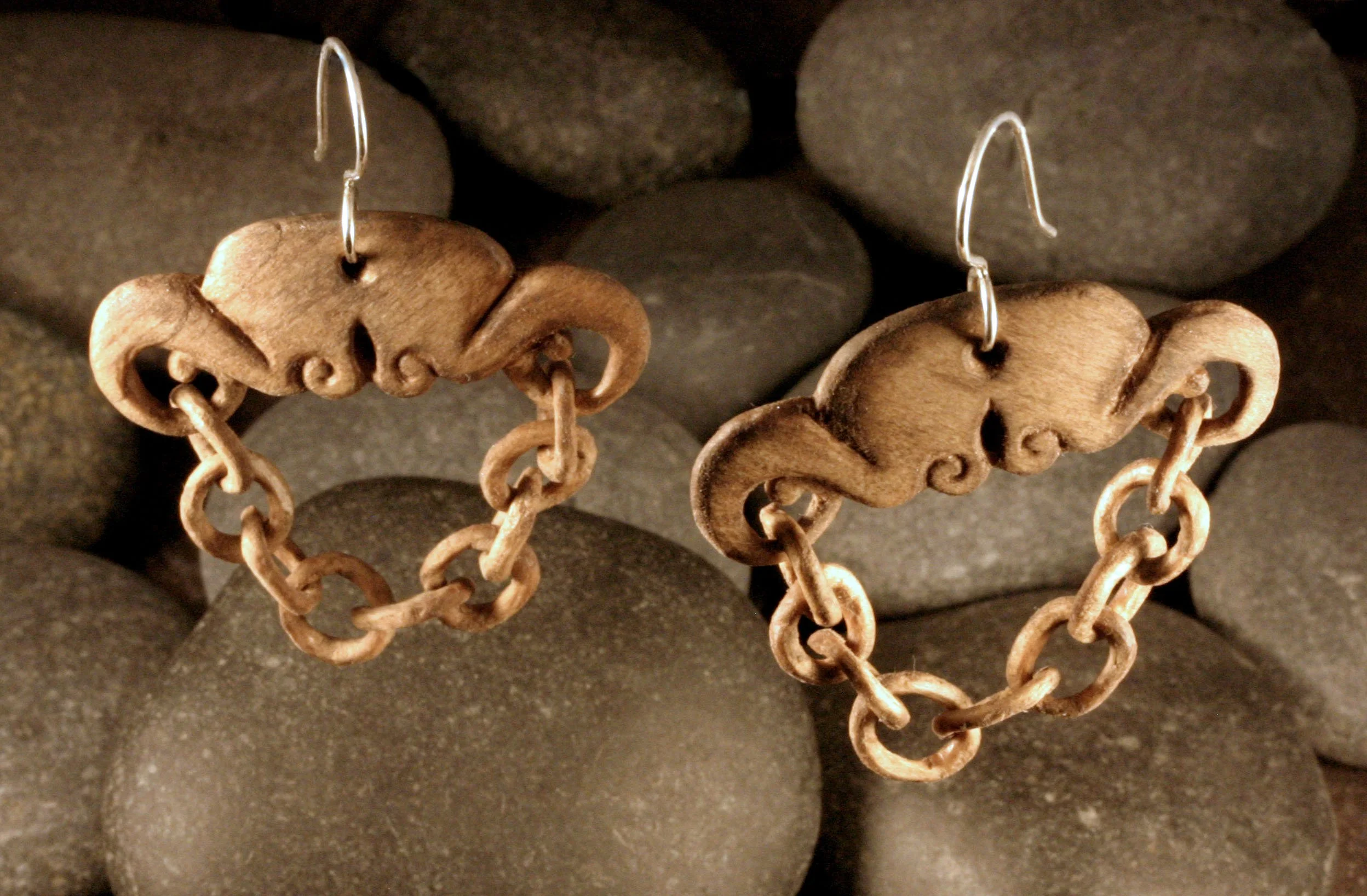 Hand carved wood chain earrings with sterling silver french hooks in front of rocks.