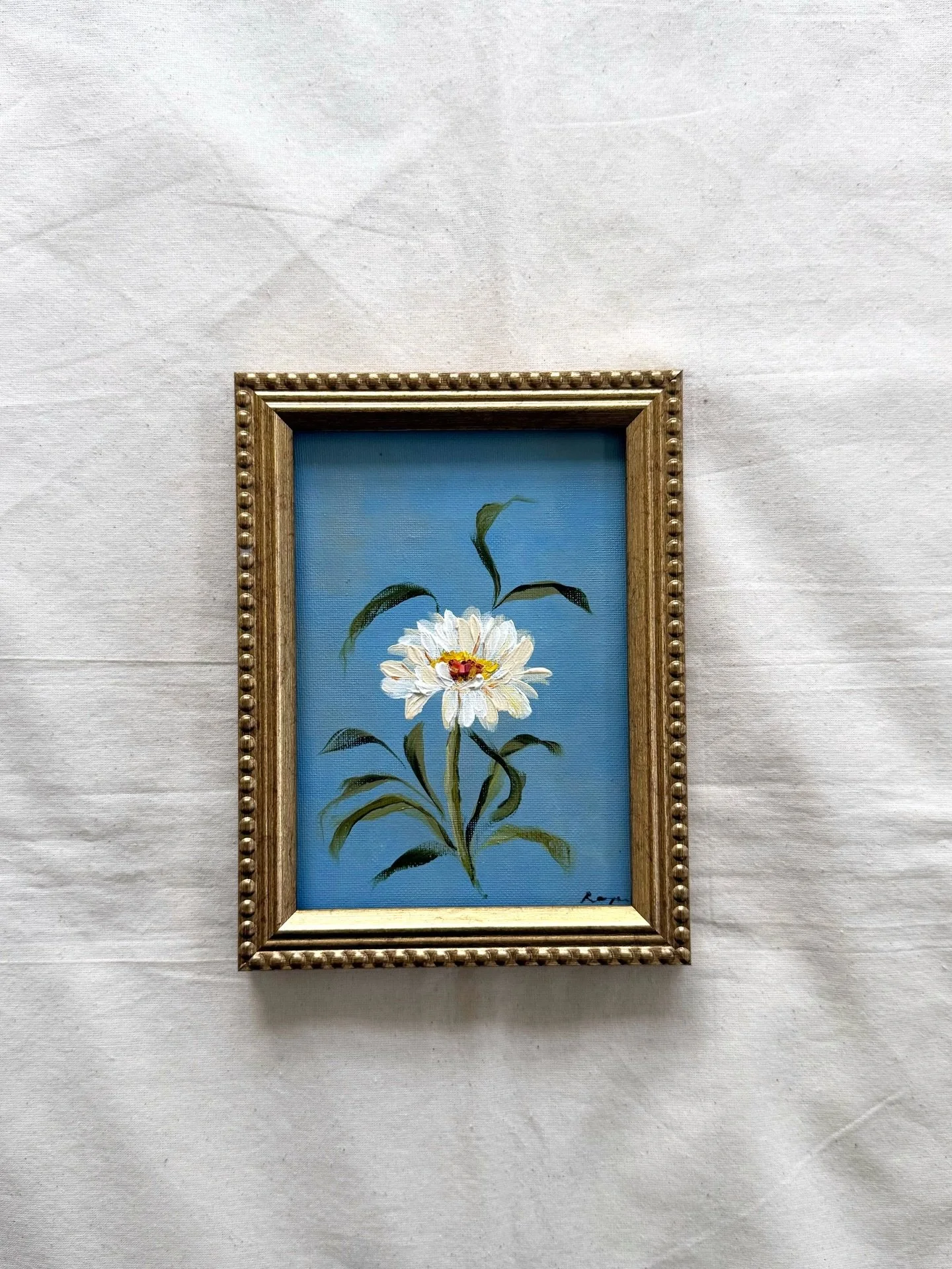 New original is live! 

This one is small but mighty.
Daisy: April Floral, 5&times;7 acrylic on canvas, framed in antique gold. A white daisy on dusty blue, painted the way I think of strength: unhurried, unadorned, completely sure of itself.
If you&