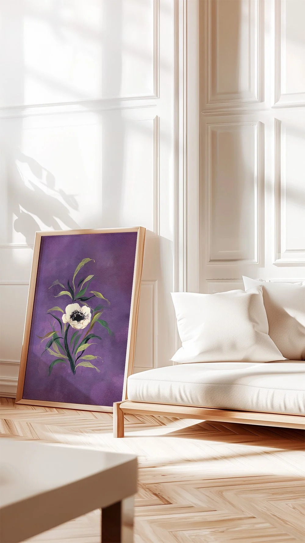 Moody violet floral wall art print leaning against a white paneled wall next to a modern cream sofa with natural sunlight shadows.
