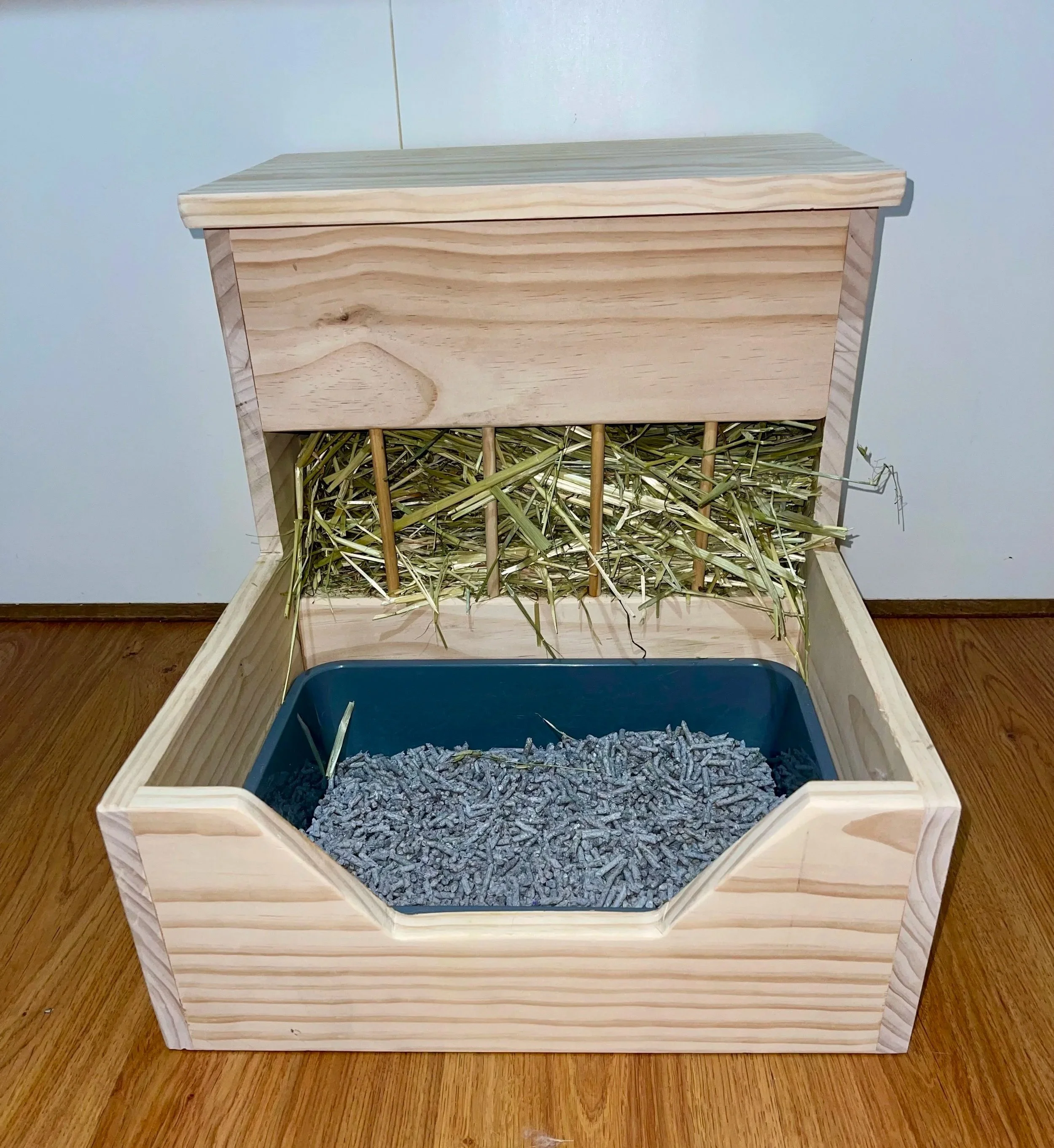 A small wooden house with a sloped roof, filled with straw and small rocks, situated on a hardwood floor.