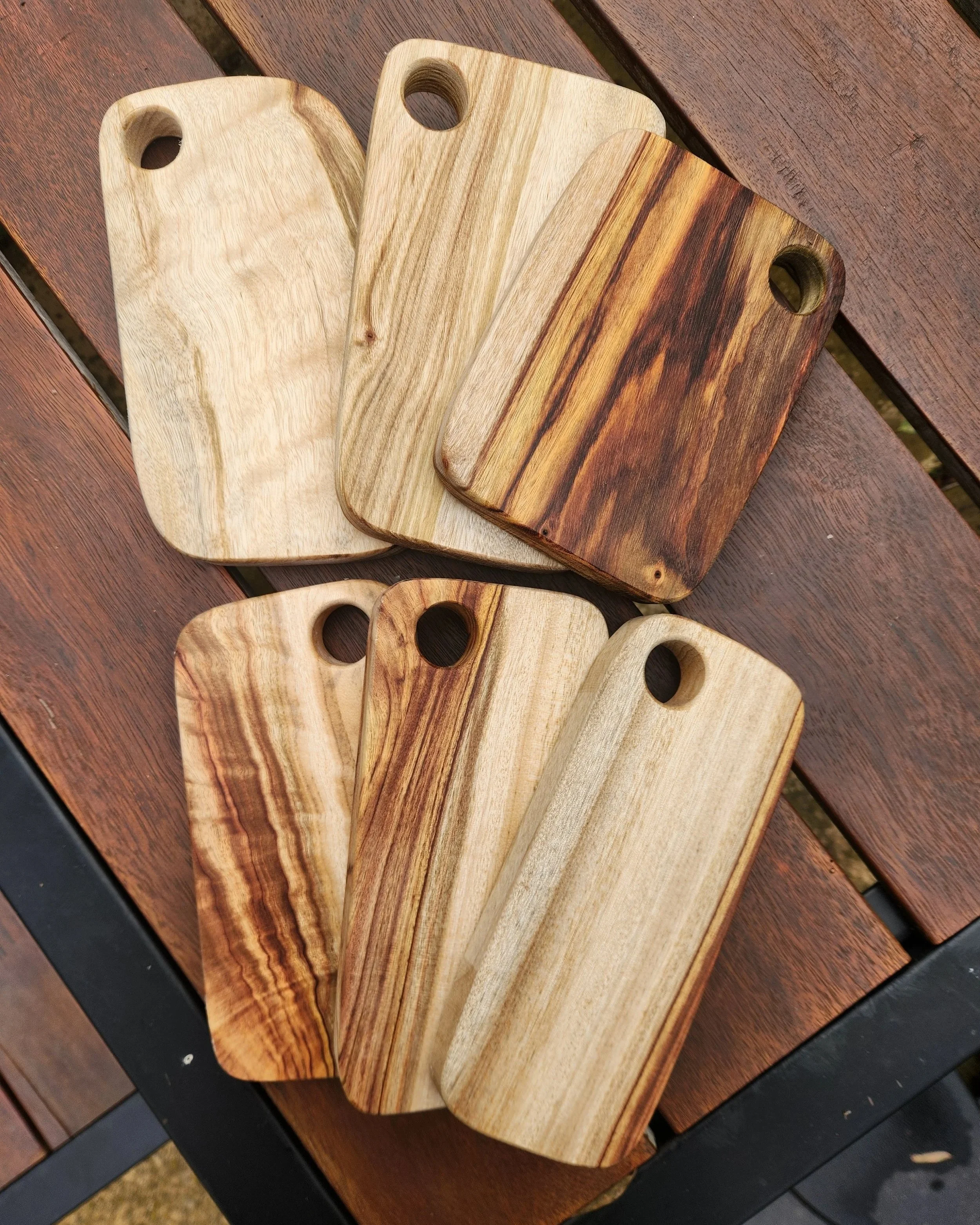 Three wooden cutting boards with a circular handle hole in each, placed on a wooden table with a dark edge.