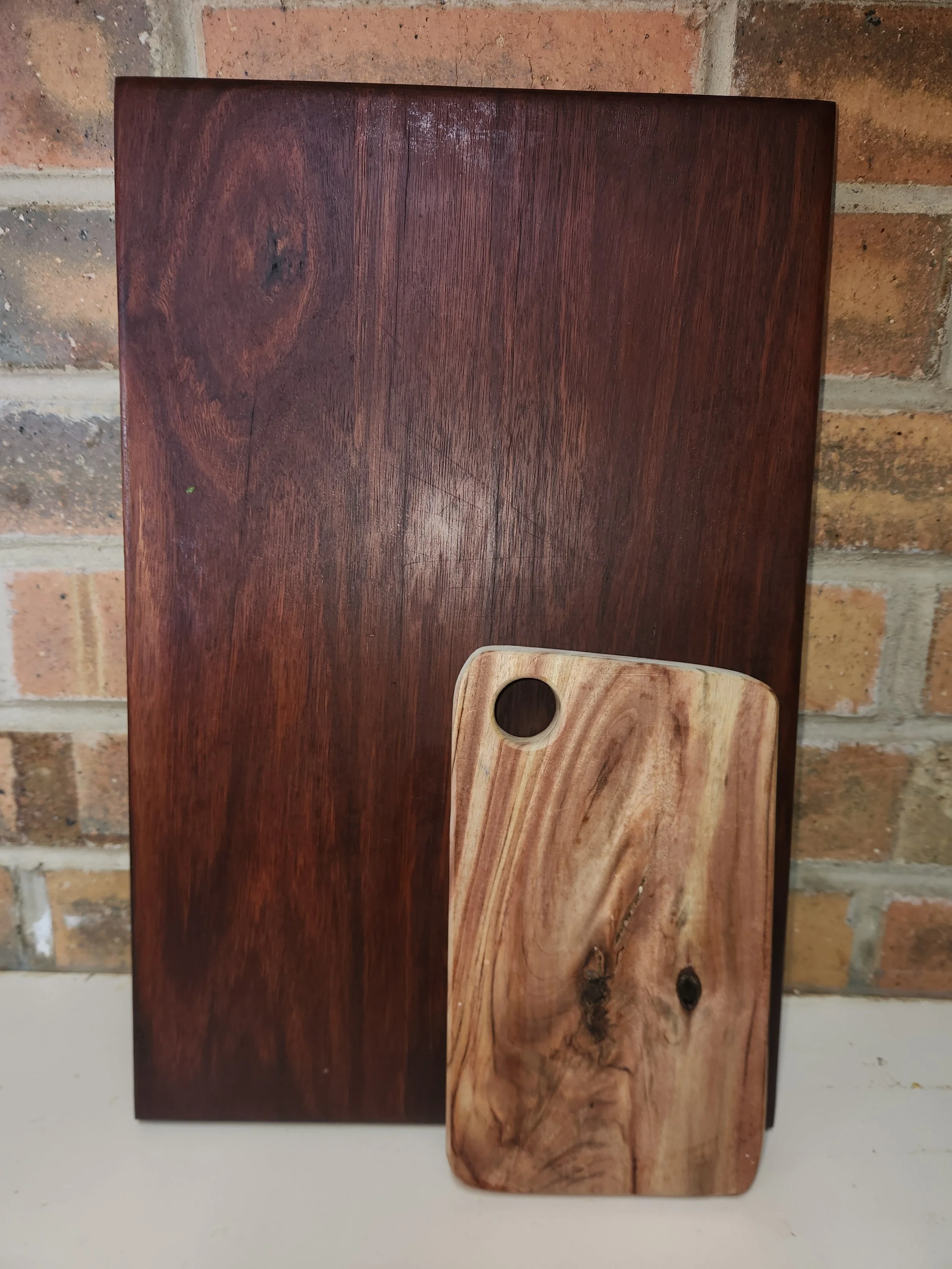 Two wooden cutting boards, one dark and one light, placed on a brick wall background.