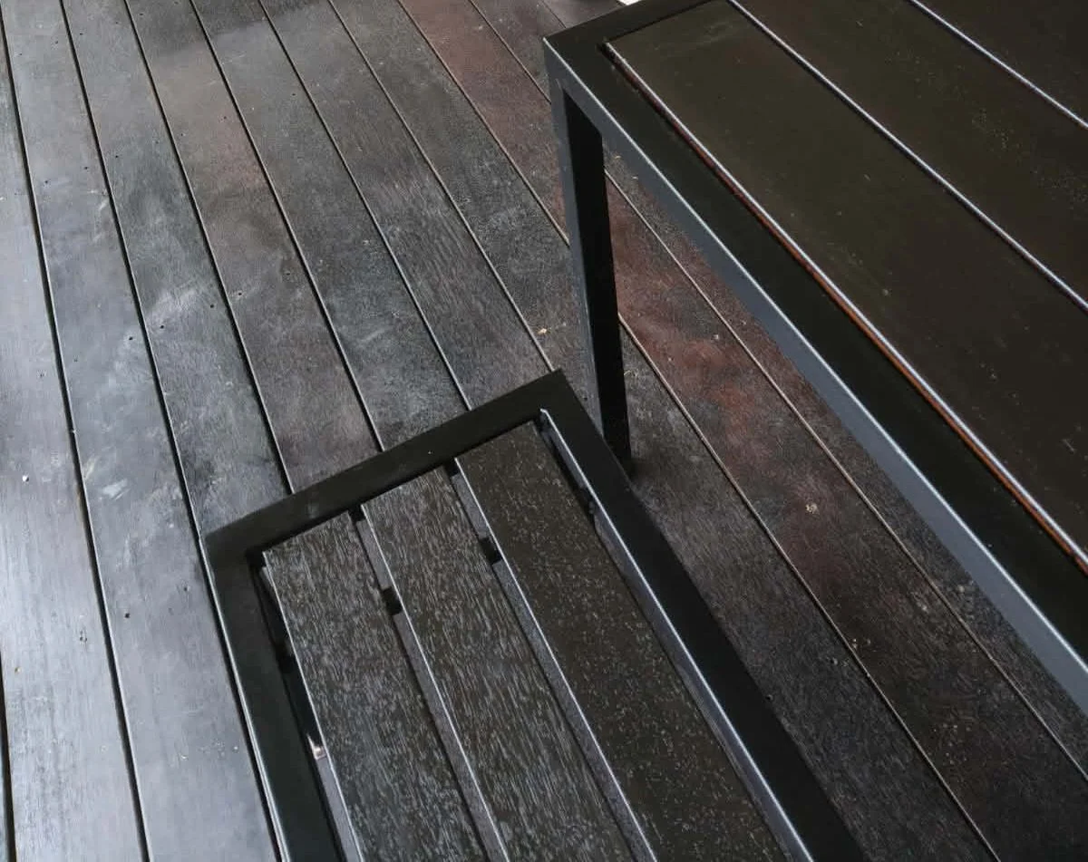 A black metal chair with wooden slats is on a wooden deck with a matching black wooden table.