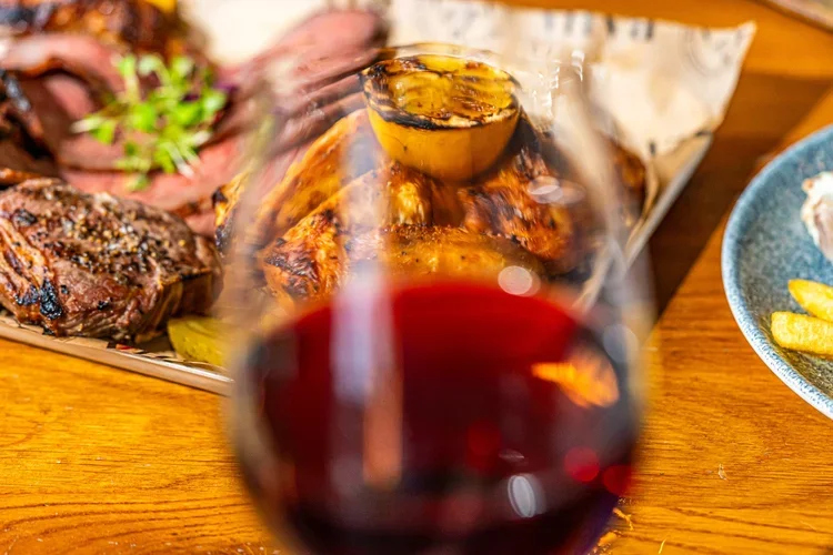 Glass of red wine on table with meat at Bowness on Windermere Pubs