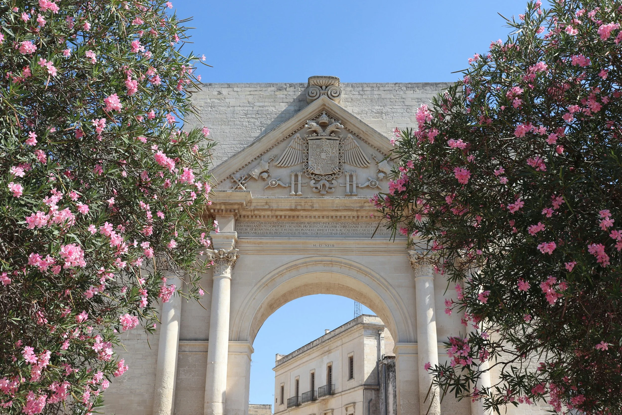 Baroque city gate in Lecce framed by pink oleander