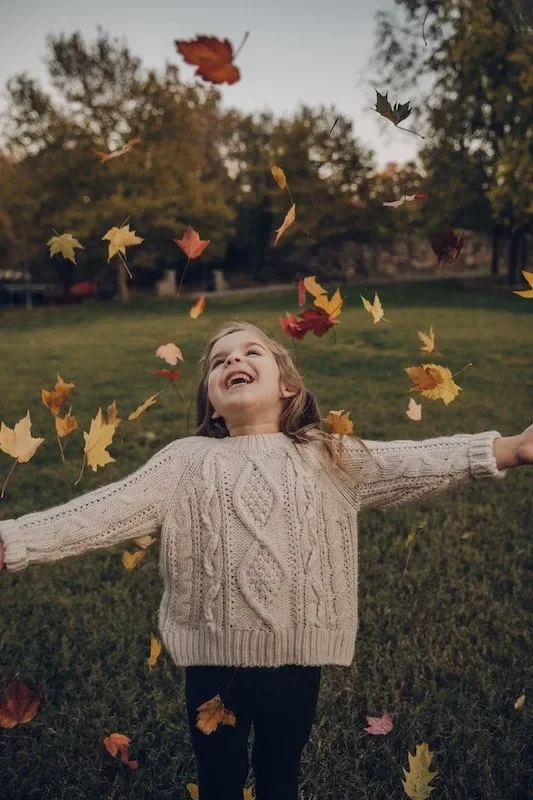 a little girl playing in the leaves