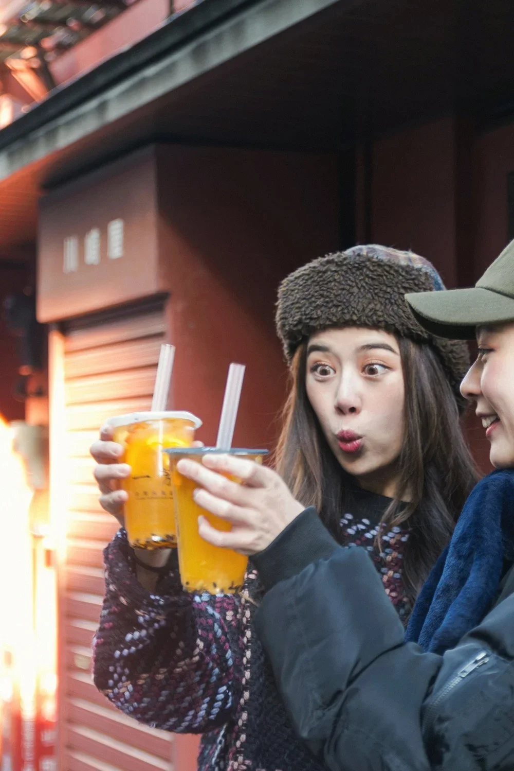 two young women wearing winter clothing with excited expressions holding cups of fruit tea in asakusa tokyo