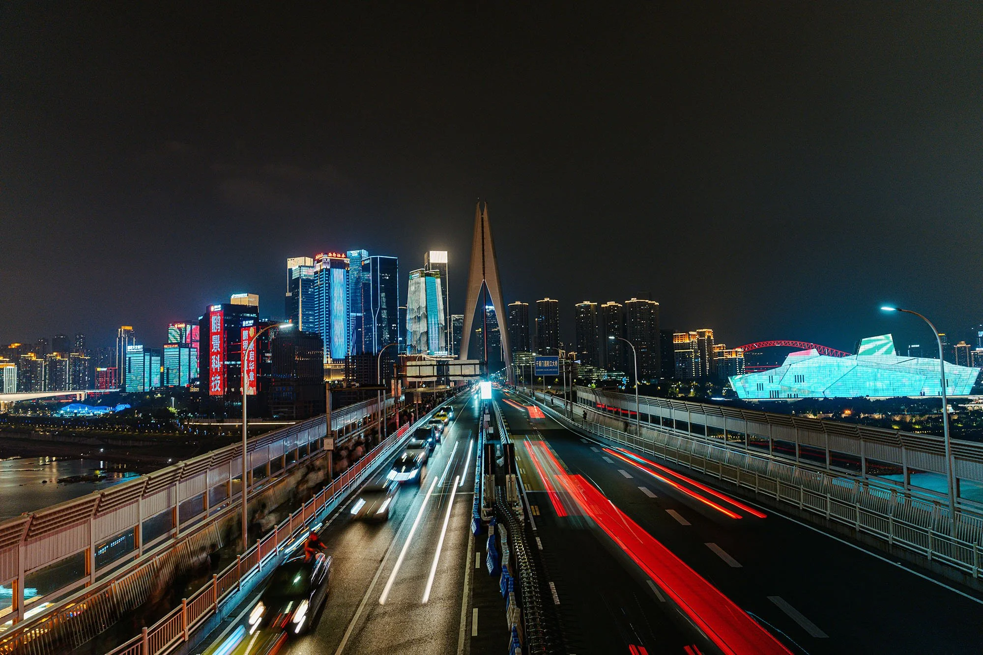 car lights streaking over the qiansimen bridge in chongqing china at night with illuminated skyscrapers and buildings on the other side of the river
