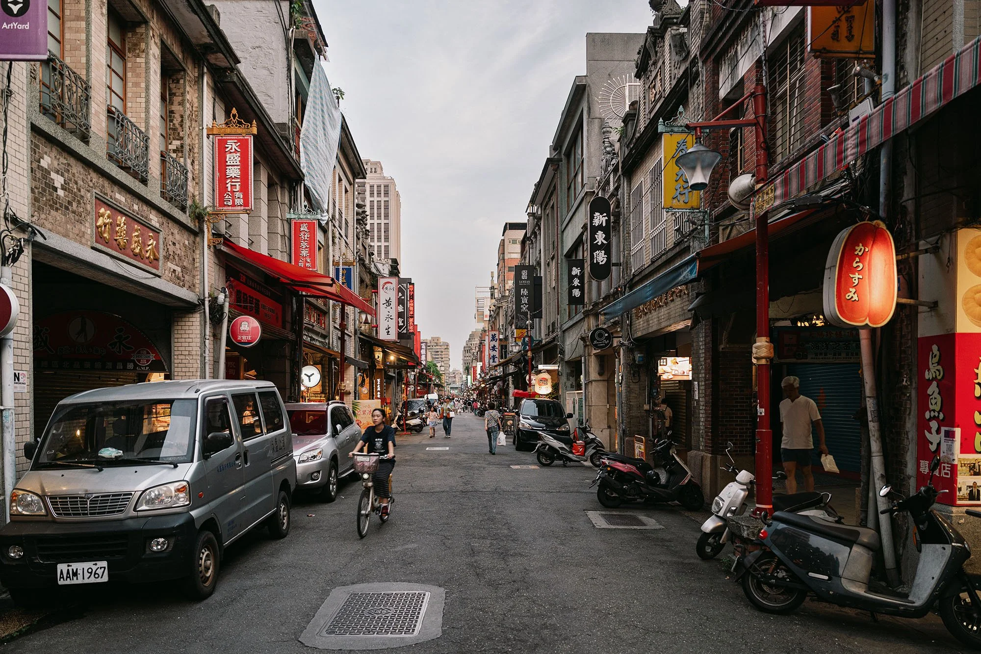 woman riding bicycle on old street lined with signs in chinese characters in taipei
