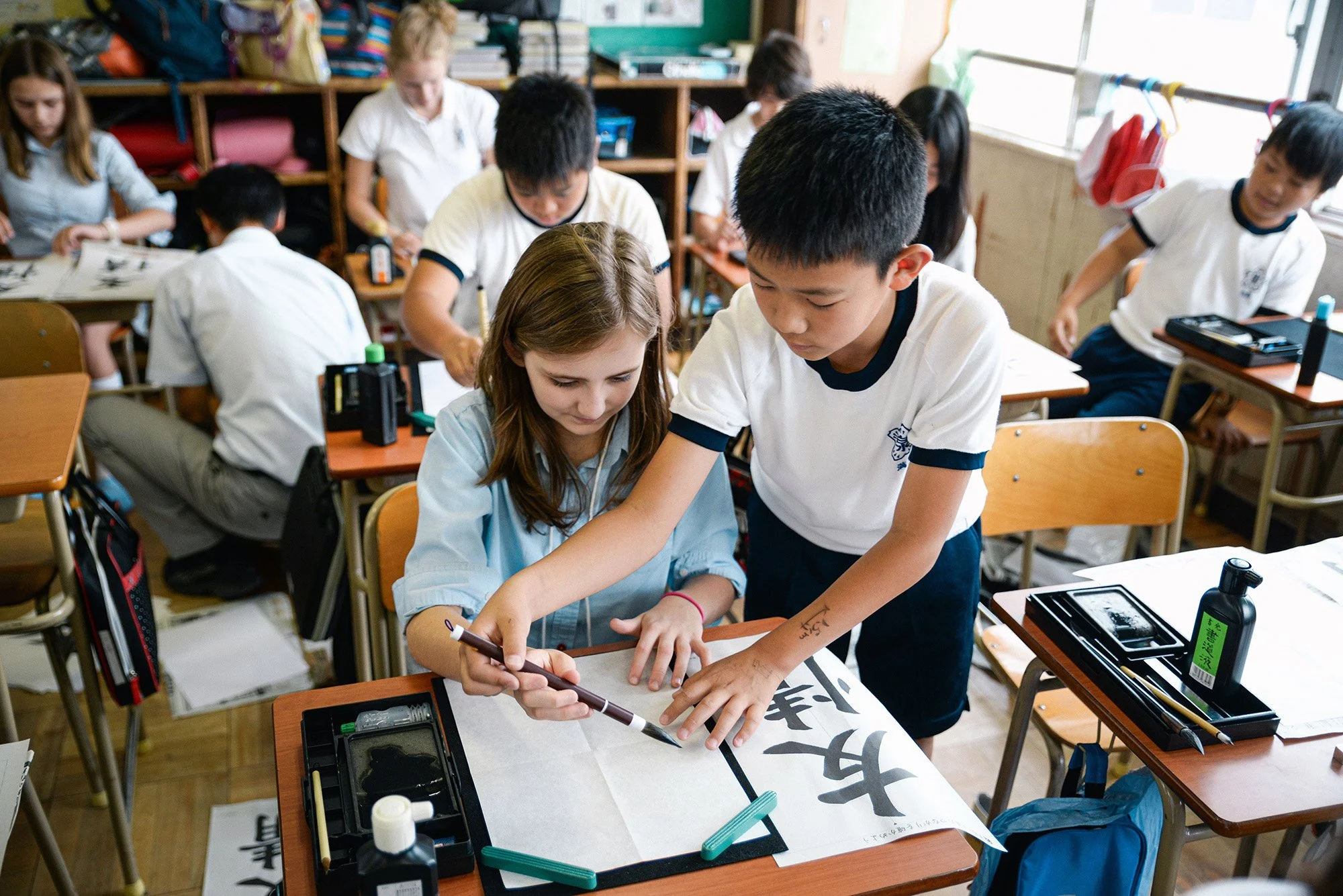 A young Japanese student helps teach calligraphy to an American student at school in Japan