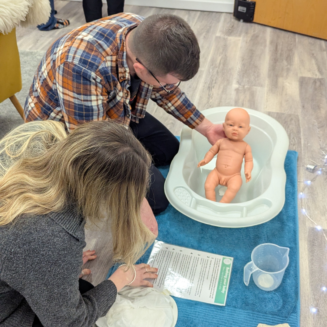 An pregnant woman and her birth partner prepare for postnatal life by practising bathing a baby safely