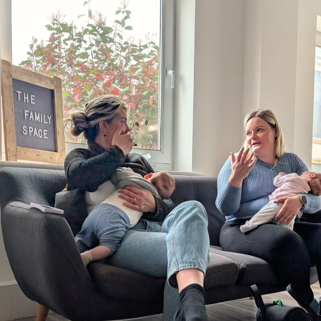 Two new mums make friends while chatting on the sofa at The Nest as their babies feed and sleep in their arms