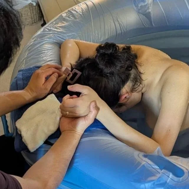 a birth partner holds the hands of a labouring woman in a birth pool at their homebirth in Cornwall supported by Gemma Kitto doula from Born to Birth Cornwall