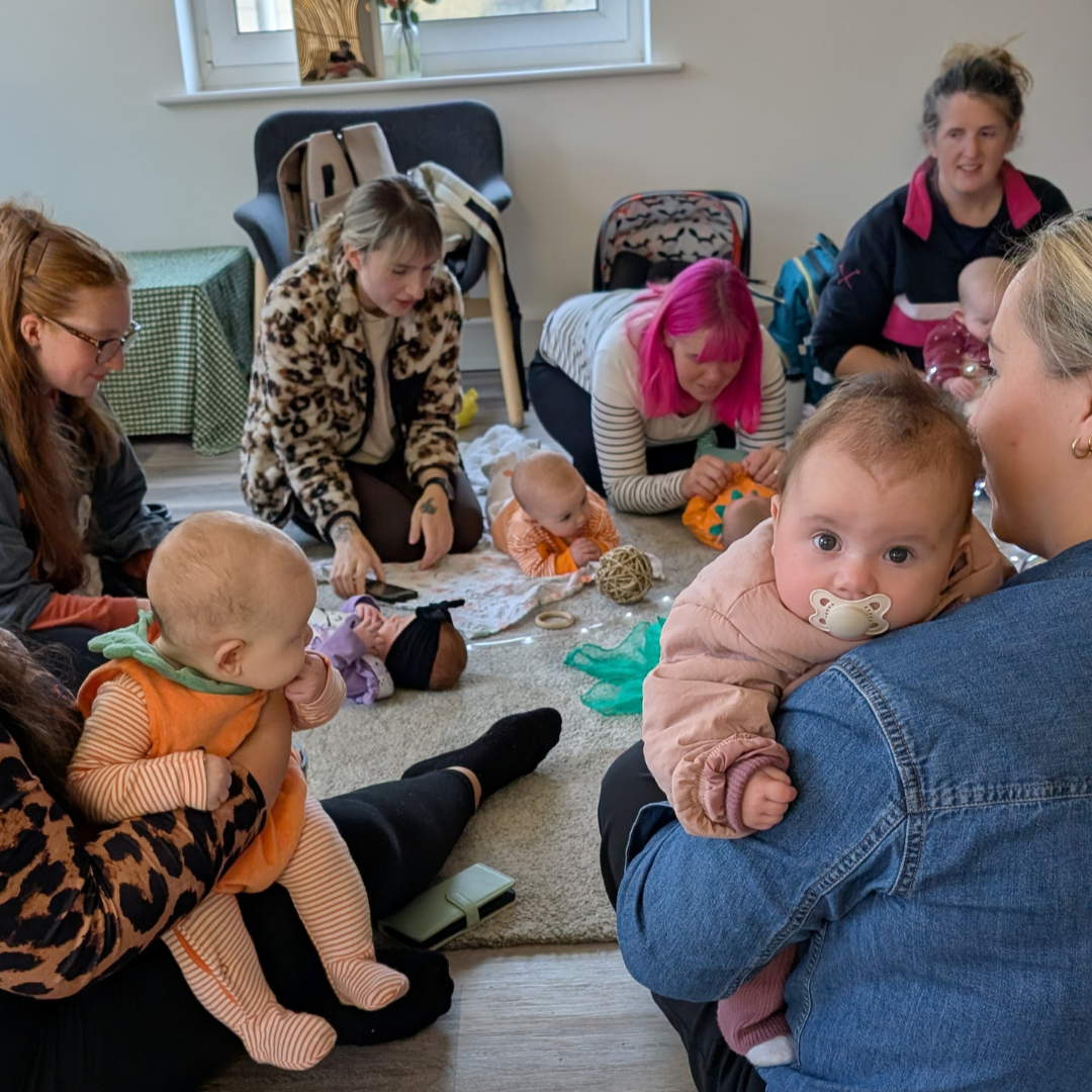 A group of new mums at the nest talk and laugh while their babies relax and play
