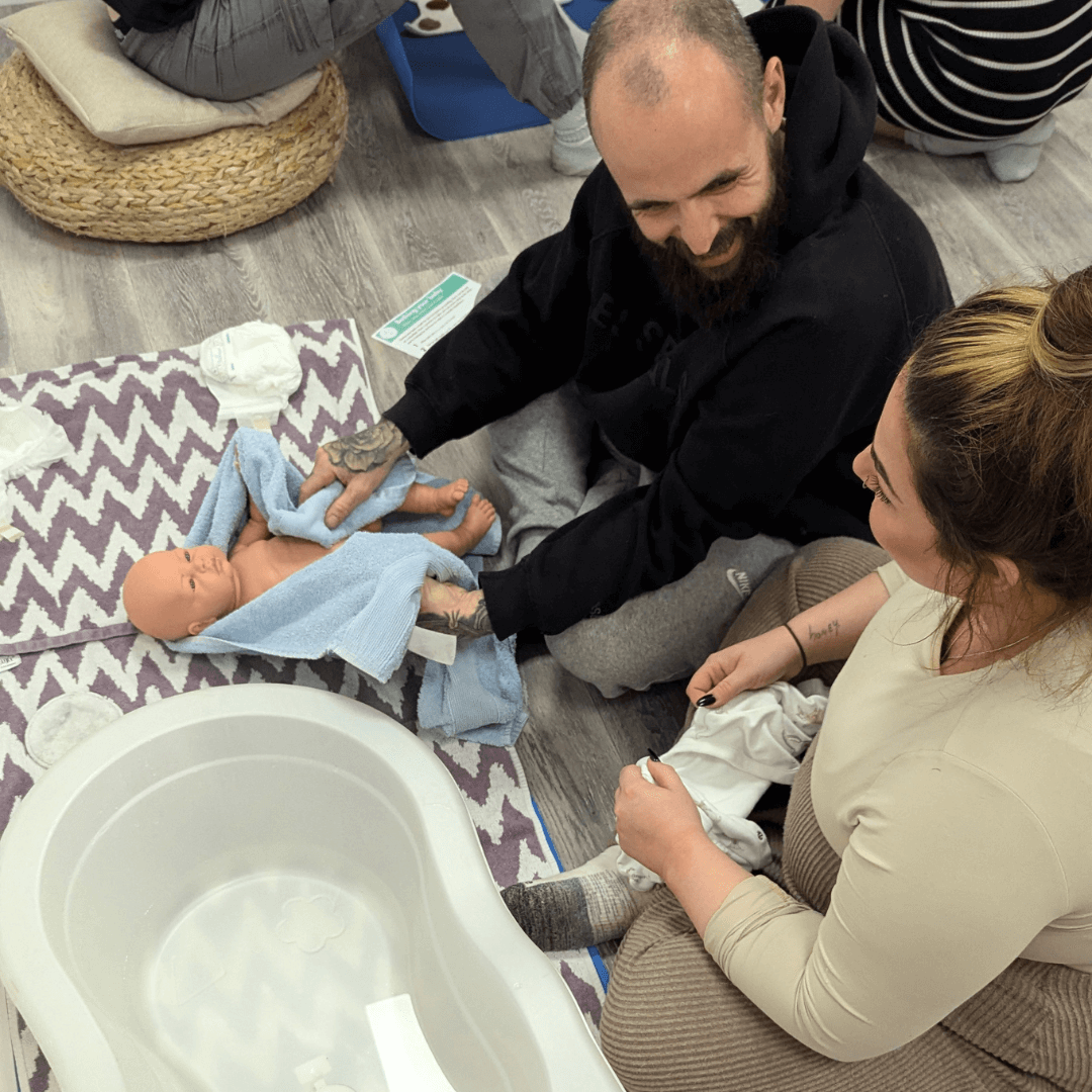 a pair of expectant parents practice bathing a baby at their group antenatal class in truro
