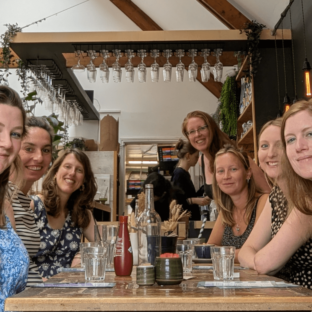 Group of pregnant people having a lively and social discussion around a wooden table at Bump Brunch in a cafe in Cornwall