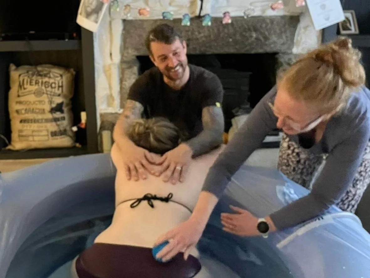 Gemma Kitto a birth doula for born to birth cornwall massages a labouring woman's back as she sits in her birth pool during birth in Redruth Cornwall