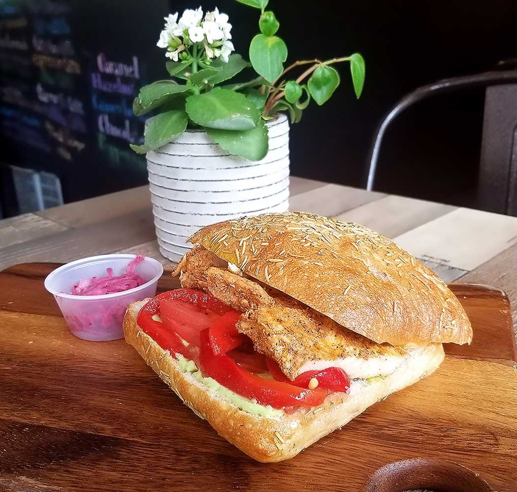 Our Grilled Chicken Sandwich plated with a side of our Pickled Onions and a flowering plant behind.
