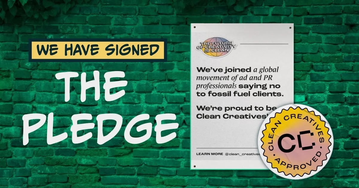 Green brick wall with a large sign that says "We have signed the pledge" and a separate poster that reads "We've joined a global movement of ad and PR professionals saying no to fossil fuel clients. We're proud to be Clean Creatives." There is a circ