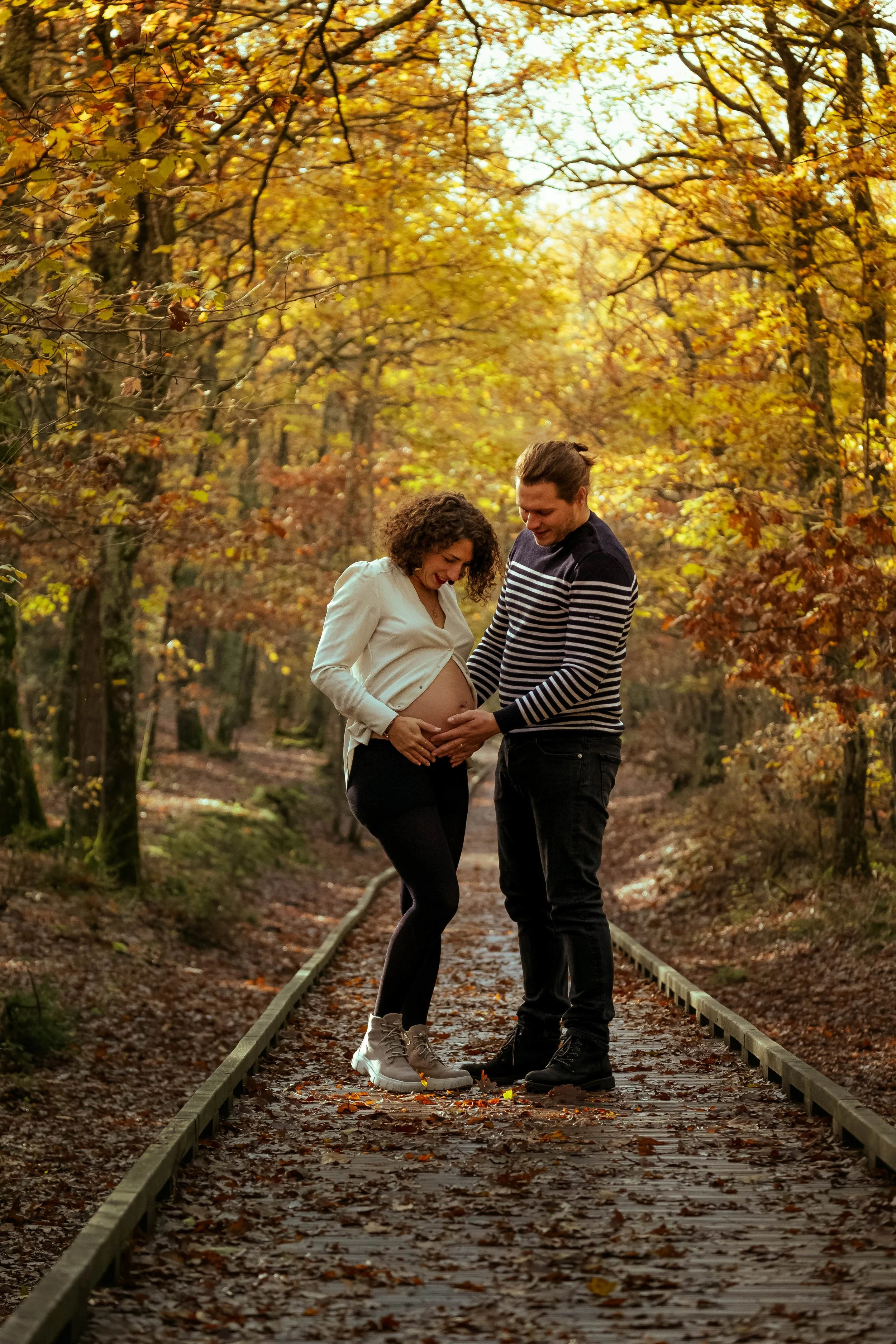 sur un chemin en bois un homme tient le ventre rond de sa femme