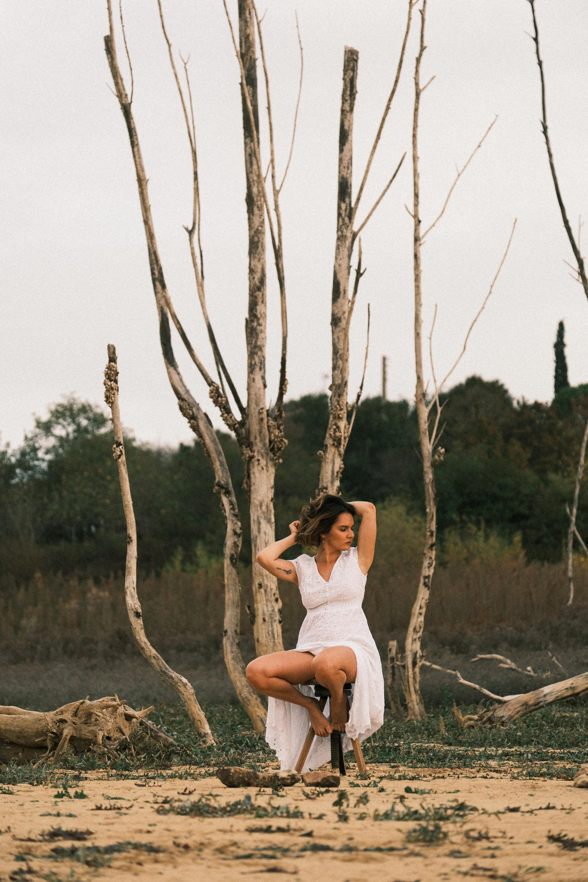 femme assise sur un tabouret dans la nature avec un arbre mort